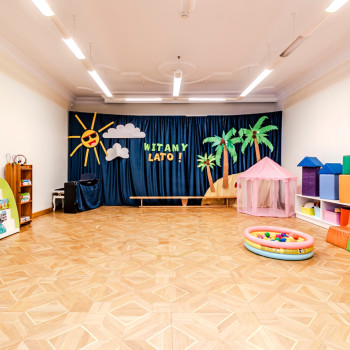 Wnętrze pomieszczenia z zieloną kotarą a na niej napis Witamy Lato